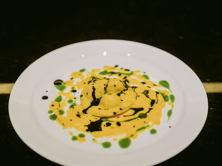 Raviolo signature dello chef Riccardo Quadri con salsa gialla e decorazioni verdi e nere.