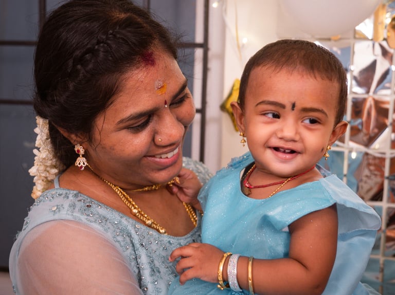 A mother in a blue lehenga holding her baby daughter at a first birthday celebration, photographed b