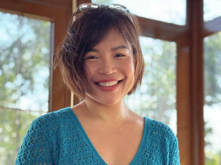 Tina in a blue sweater is smiling and holding a coffee