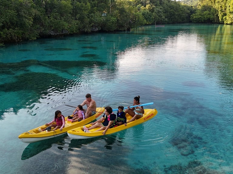 Family kayaking in yellow tandem kayaks on clear turquoise water in Kehedaing tropical lagoon.