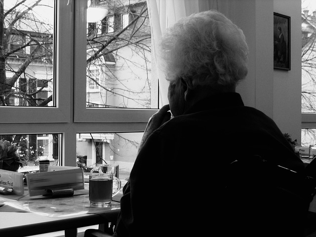 image en noir et blanc, une vieille femme regarde par la fenêtre
