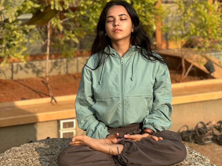A young girl practicing mindful meditation in a lotus yoga pose on a large rock outdoors.