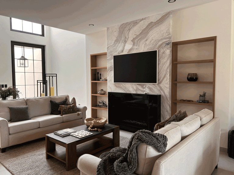 Sala con chimenea revestida en mármol, muebles neutros y estanterías de madera integradas | KARÄNA
