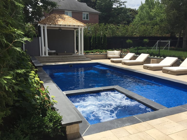 Luxury backyard swimming pool with built-in hot tub, poolside lounge chairs, and a white pillared gazebo.