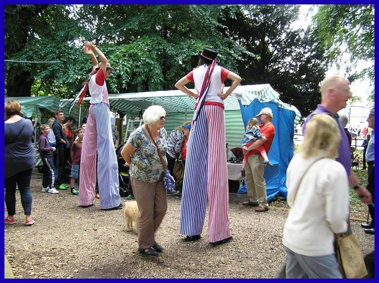 Performers on stilts in red white and blue striped costumes entertain crowds at an outdoor festival.
