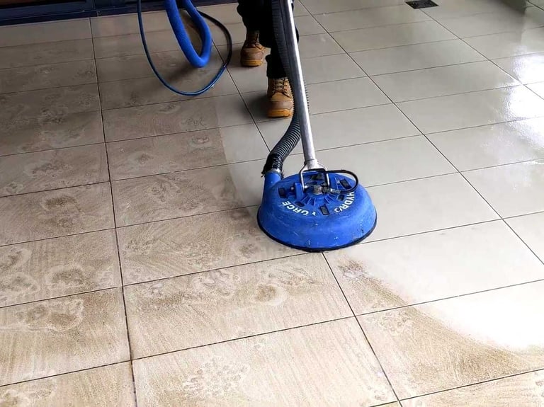 Professional floor cleaner using a rotary pressure tool to deep clean dirty ceramic tile and grout.