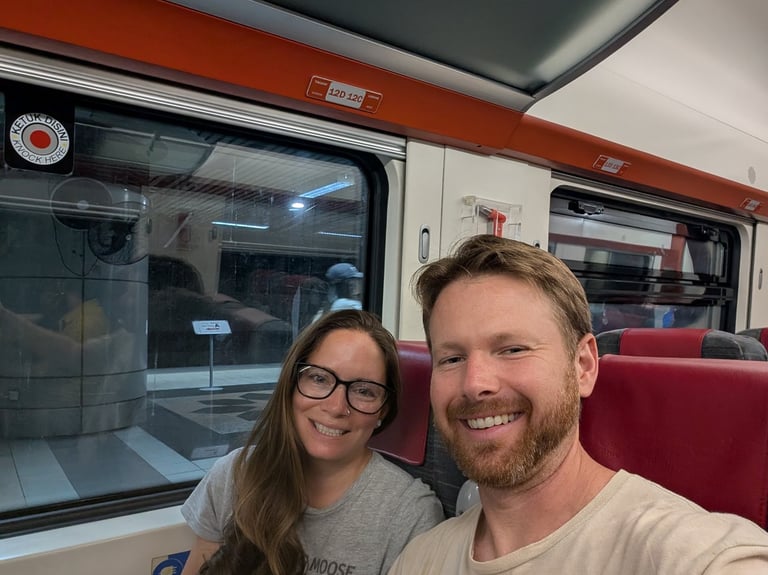 Don & Samantha weaing Traveling Moose and Bus shirts sitting on a train with red seats during a trip.