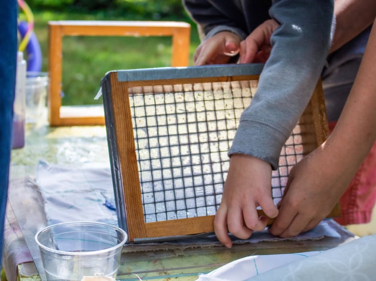 The hands of two children lifting a small screen while making paper.
