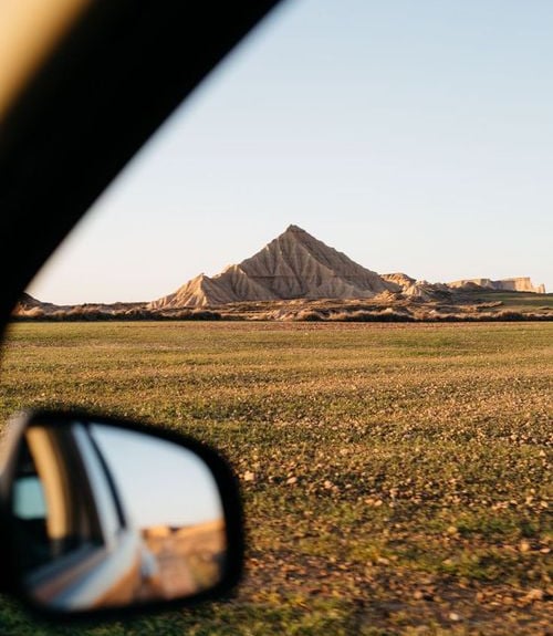 A scenic road trip view of the Bardenas Reales desert mountains through a car window at sunset.