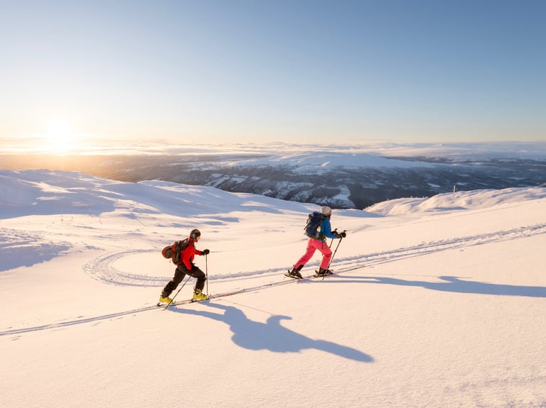 two people ski touring up the mountain during sunrise
