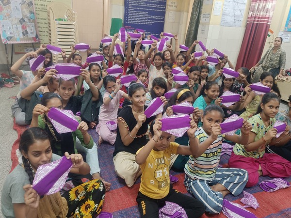 Group of about forty girls sitting on the floor holding up fabric sanitary napkins.