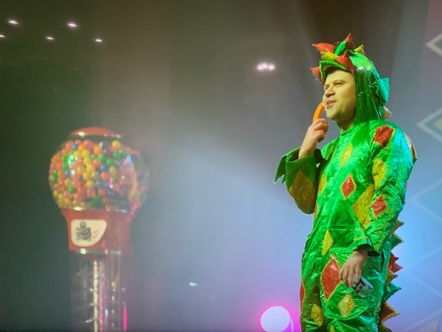 Piff the magic dragon stands on stage next to a giant lumball machine.