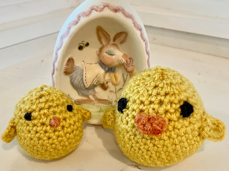 2 yellow crocheted chicks with a ceramic Easter egg behind them.