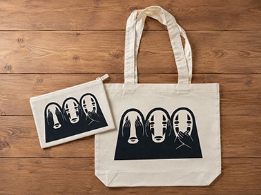 Bolso de manta y neceser a juego con estampado de No Face sobre fondo de madera.