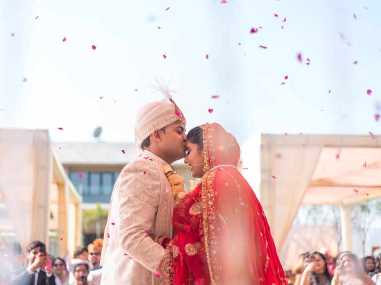 Bride and groom in traditional wedding attire share a tender moment with falling petals.