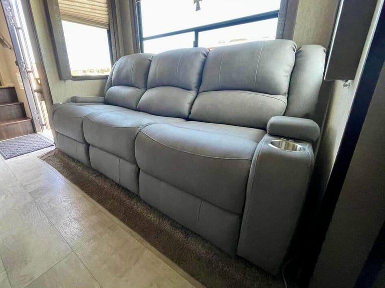 Grey leather reclining sofa with cup holders inside a modern luxury RV living area.