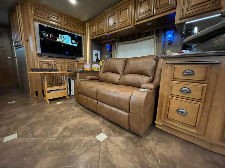 Luxurious RV interior featuring a brown leather recliner sofa, custom wood cabinets, and a flat-screen TV.
