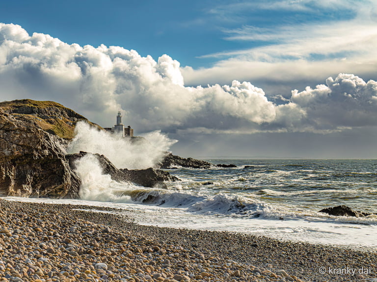 a lighthouse on a rocky beach with waves crashing over the rocks