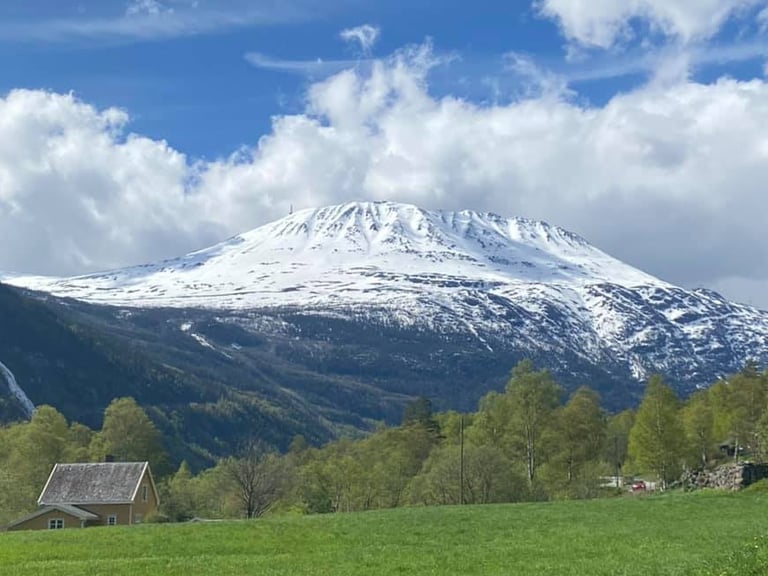 snow covered mount gausta with treeline and house and in the foreground