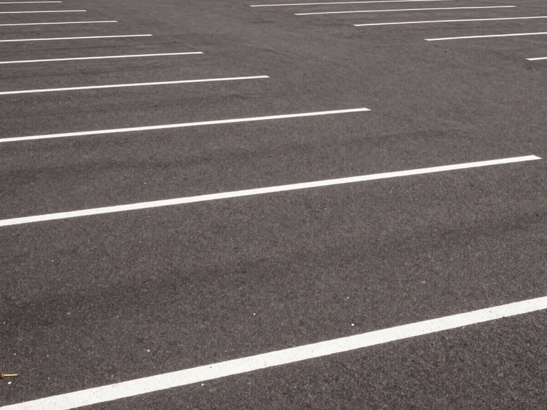 Wide environmental shot of a freshly striped commercial parking lot with crisp white lines under bright midday sun, 35mm