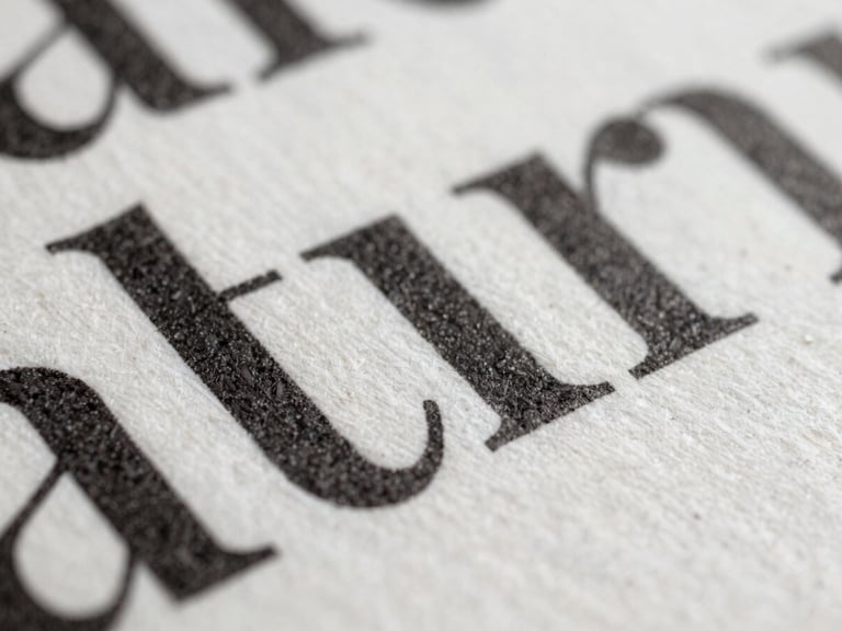 A macro close-up of a heavy cotton paper page, deeply debossed black ink typography, soft north-facing daylight casting subtle shadows across the texture.