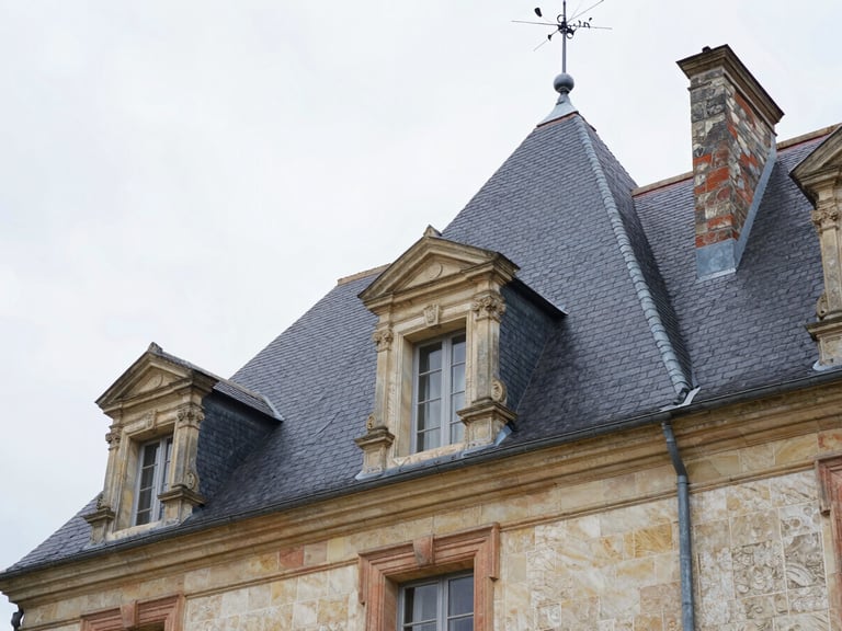 Low-angle shot of a grand French country house with a newly completed dark slate roof, soft overcast light, sharp architectural details
