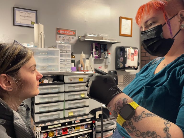 Professional piercer wearing a face mask and gloves discusses piercing aftercare with a client.
