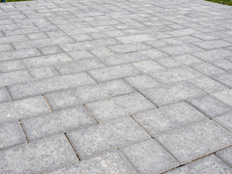 Wide shot of a newly installed grey block paving patio with crisp edges, bright overcast daylight, natural colors with sharp contrast, 35mm