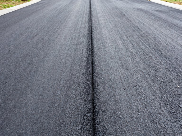Detail shot of a new asphalt driveway with a visible drainage channel, bright overcast daylight, natural colors with sharp contrast, 35mm