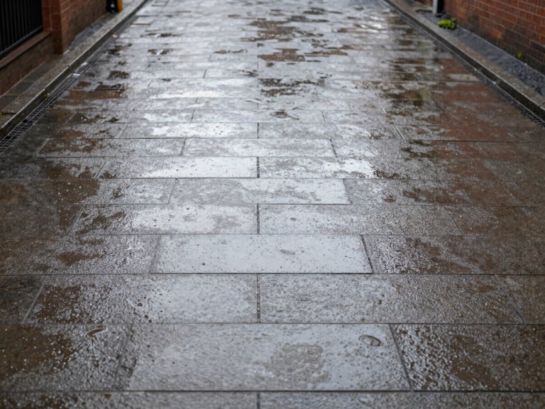 Wide environmental shot of a pristine, freshly cleaned block-paving driveway in a Liverpool suburb, wet stones reflecting bright overcast daylight, 35mm.
