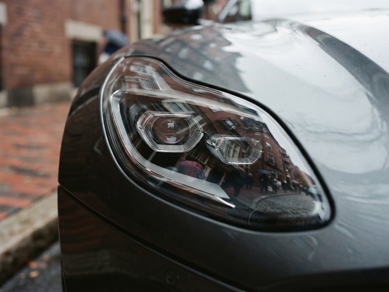 Close-up of a modern luxury vehicle headlight reflecting historic Boston brick architecture on Charles Street, overcast daylight, 35mm photography