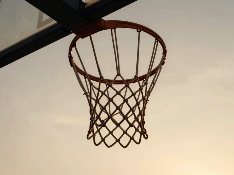 Low-angle heroic shot of a basketball net against a warm golden hour sky, high contrast, cinematic 35mm