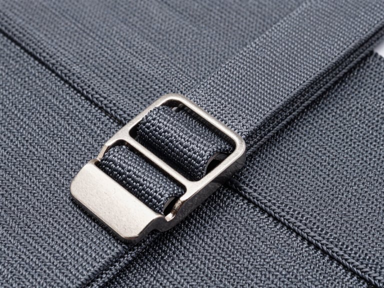 Close-up of heavy-duty slate gray equestrian webbing, showing dense weave structure, stainless steel buckle attachment, high-contrast industrial lighting