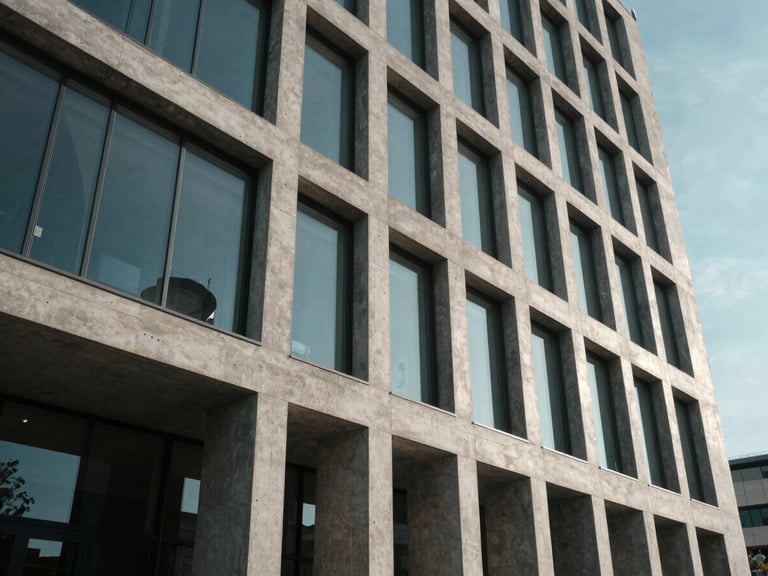 Wide-angle architectural elevation of a modern concrete and glass facade under high-contrast, cool-toned daylight with sharp shadows.
