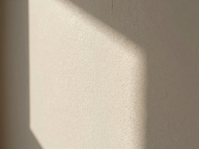 Close-up of a limewash wall texture in warm off-white, soft natural light, architectural shadows, extreme detail.