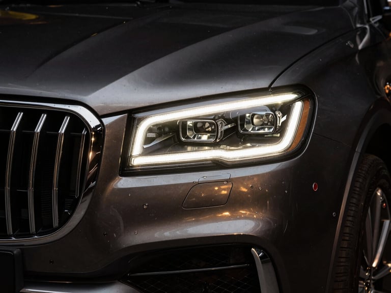 Dramatic close-up of a polished chrome grille and LED headlight of a luxury SUV, low-key studio lighting, gold reflections