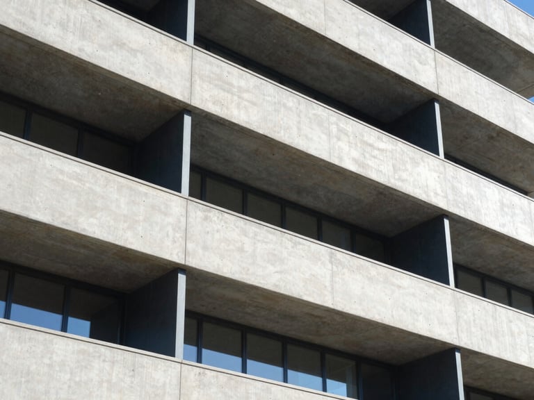 Sharp architectural drawing overlaid on a modern concrete and steel building facade, bright daylight, high contrast shadows