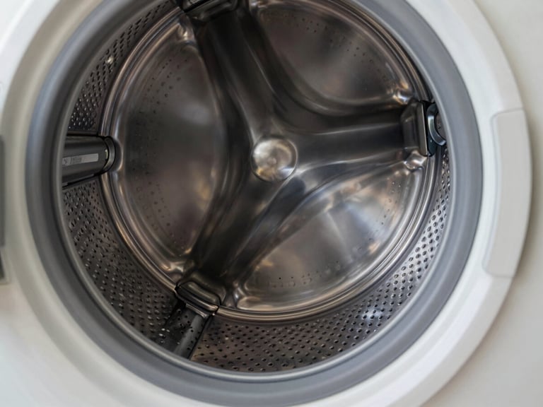 Close-up of a modern stainless steel washing machine drum interior, clean metallic reflections, sharp focus on the drum pattern, bright daylight