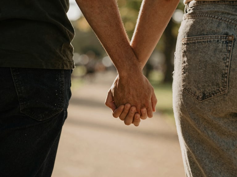 A close-up shot of a couple walking together in a sunlit park in Lyon, hands gently touching, warm natural lighting, shallow depth of field, authentic connection.