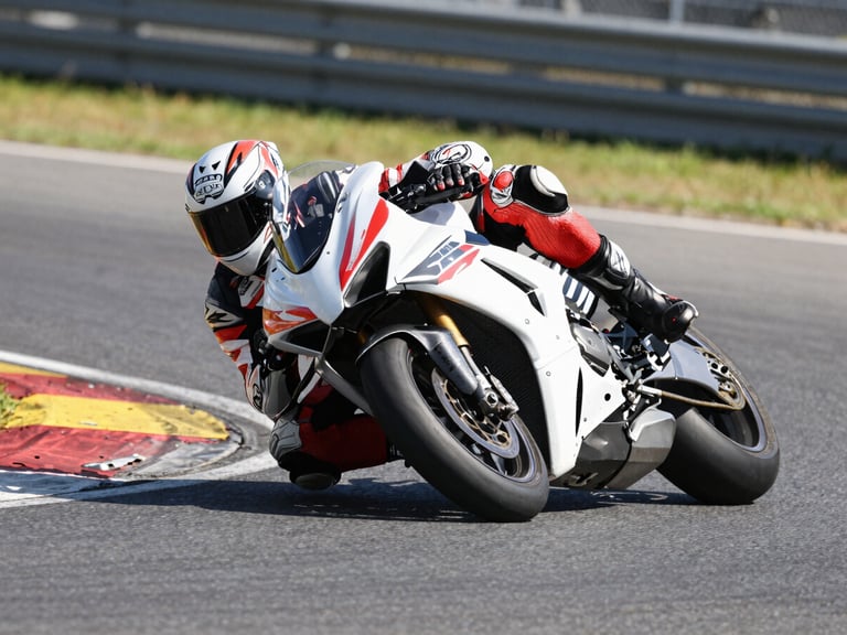 Low-angle wide dynamic shot of a superbike leaning deep into turn four under harsh midday sun, knee slider scraping the high-friction asphalt, motion blur on the background.