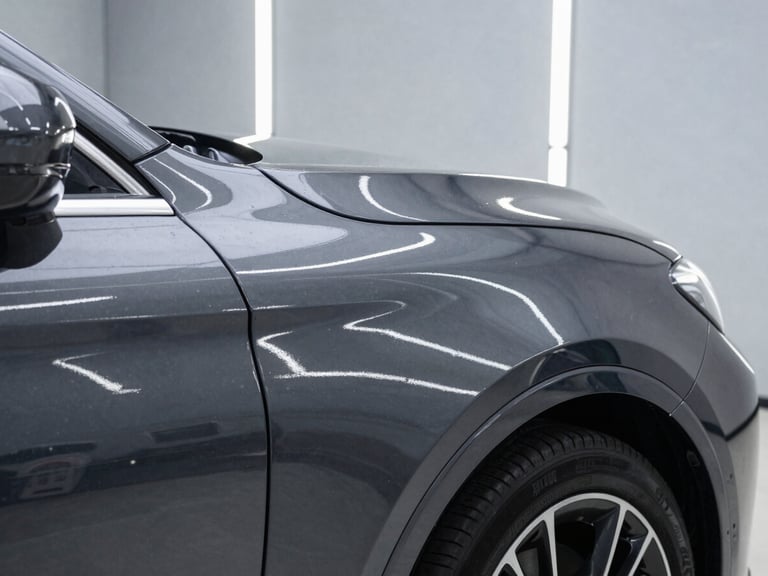 Close-up of a high-end car fender with a flawless, mirror-like dark grey paint finish reflecting bright, linear LED strip lights of an immaculate workshop