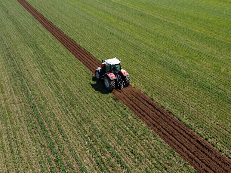 Wide aerial drone shot of a tractor cultivating a vast field, creating precise furrows, commercial agriculture photography, bright direct sunlight