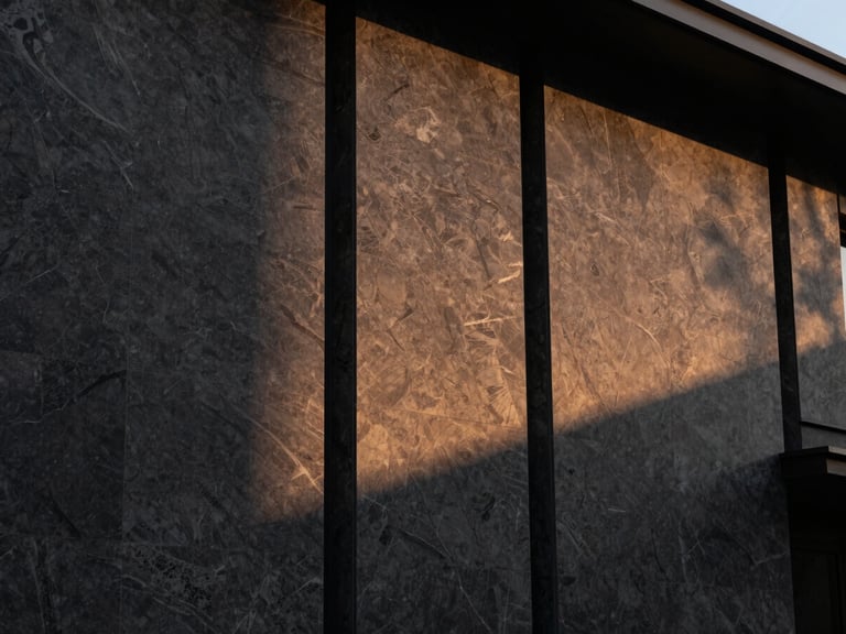 Modern luxury villa facade with dark textured granite wall cladding, sunset side-lighting highlighting the natural cleft finish, architectural photography