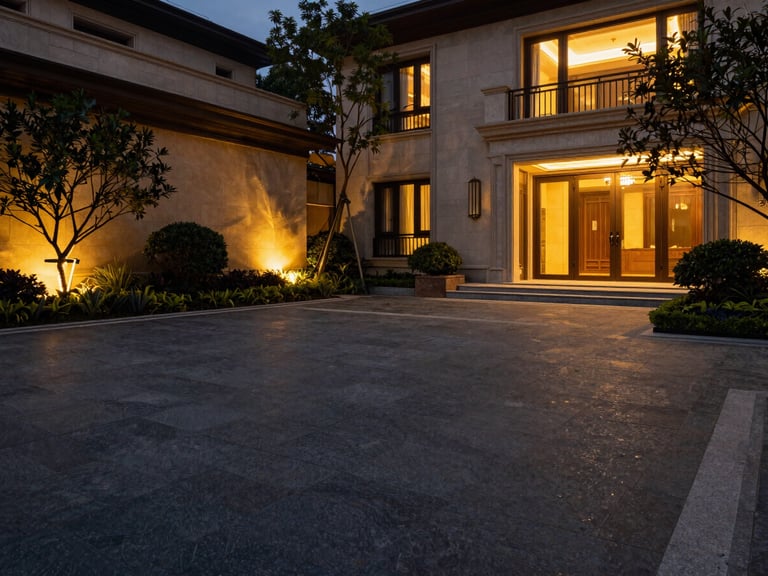 Expansive architectural wide shot of a luxury villa courtyard with dark stone paving, manicured greenery, and warm golden lighting highlights, 35mm