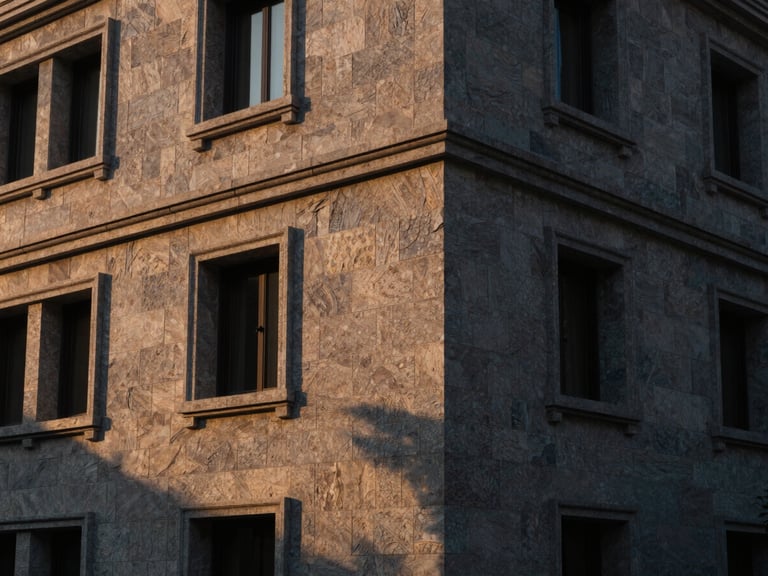 Wide-angle architectural photograph of a luxury residential facade clad in hand-dressed natural grey stone, warm sunset light casting long dramatic shadows, showcasing texture and depth