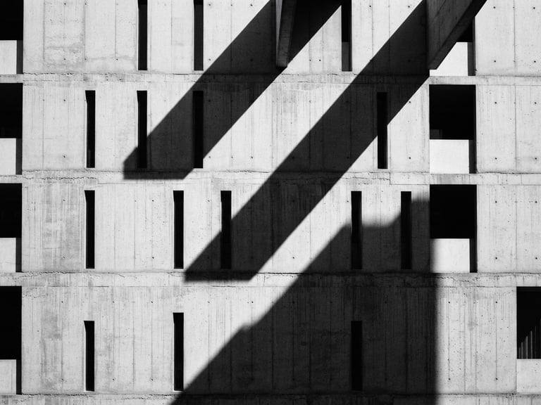 High-contrast monochrome architectural shot of a minimalist concrete building facade, sharp diagonal shadows, dramatic key light, 35mm film grain.