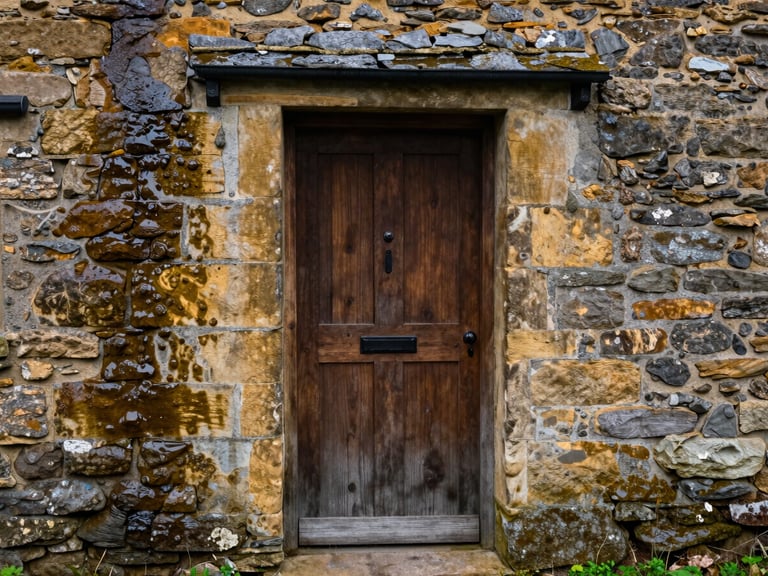 Detail of hand-dressed local stone around a newly installed timber door on a restored Yorkshire cottage, damp stone showing rich texture.
