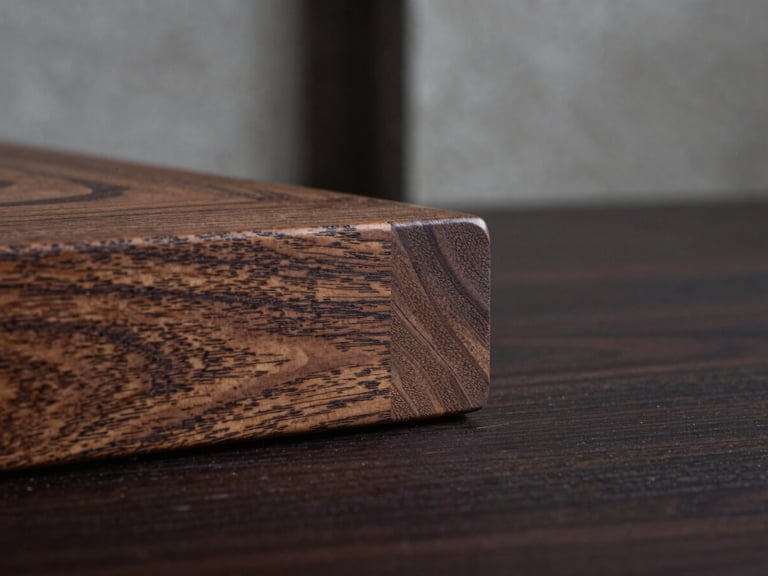 Extreme macro close-up of a Japanese-style wood joinery on a dark solid oak table, dramatic side chiaroscuro lighting carving out the deep textured grain, concrete architectural background, negative space on the right.