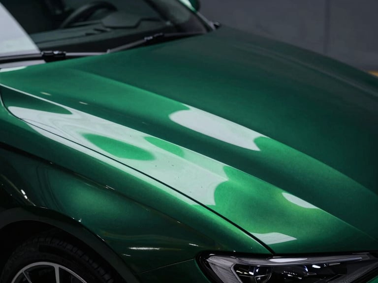 Macro shot of a pristine, deep metallic green car paint finish reflecting workshop lights, showcasing flawless surface and rich reflections, under dramatic workshop lighting, deep shadows, rich metallic reflections, 50mm lens