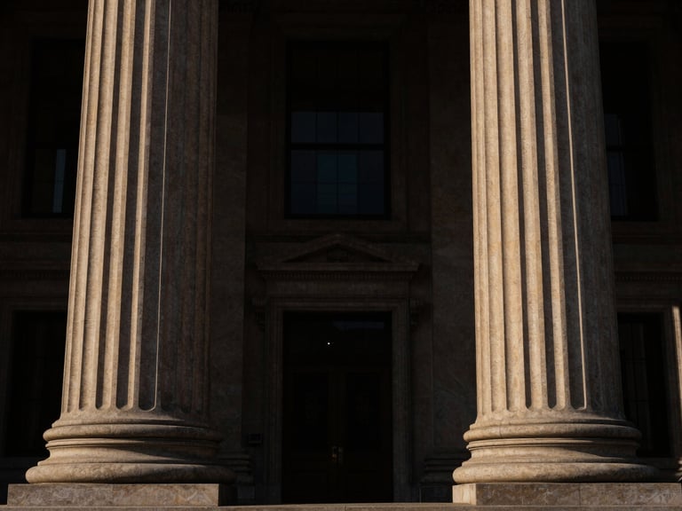 Symmetrical architectural shot of courthouse pillars, low-key dramatic side-lighting, deep brown and gold tones, high contrast, 35mm